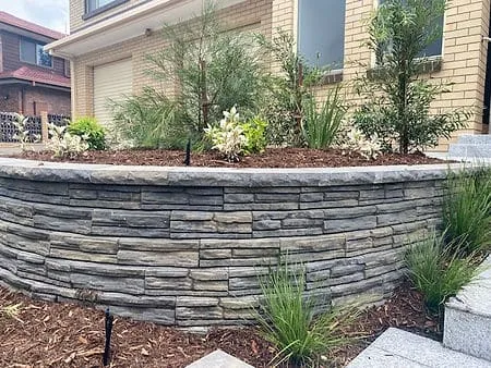 Curved stone-look retaining wall forming a raised garden bed at the front of a home